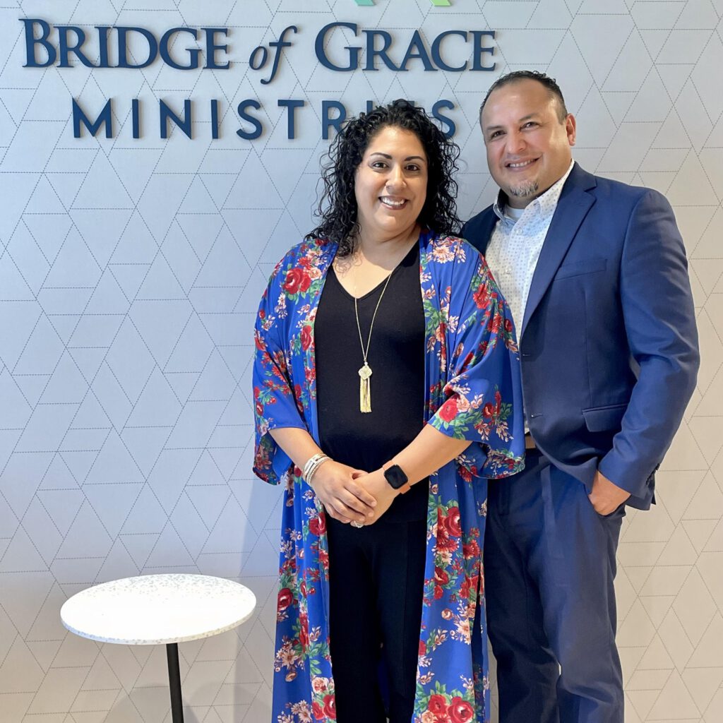 photo of Javier and Annette Mondragon in front of the Bridge of Grace Ministries office sign